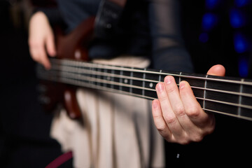 Fototapeta premium Female bassist rehearsing. Female musician with bass guitar. Female performer practicing in dim studio lighting. Female bassist preparing for performance in moody rehearsal space
