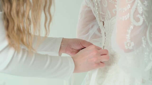 A beautiful young bride's mother ties her wedding dress, close-up