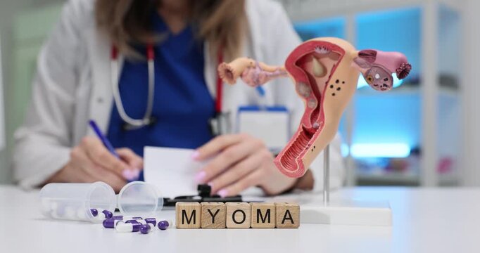 Woman gynecologist writes detailed recommendations for patient. Wooden blocks on table form word Myoma near anatomical model of uterus in clinic