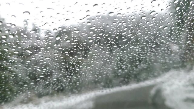 Raindrops on a car window create a pattern while a winding road is visible through the droplets in the background