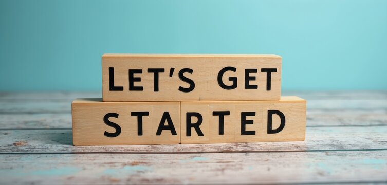Wooden blocks spell LETS GET STARTED on a textured surface against a teal background. This visual signifies beginning new ventures, projects, or phases with positive intent and readiness for action.