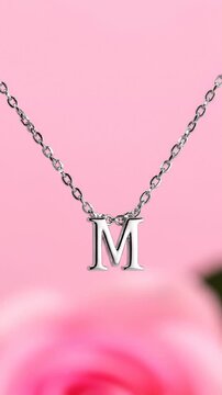 Silver Letter M Initial Pendant Necklace Hanging Against Pink Background, Close Up