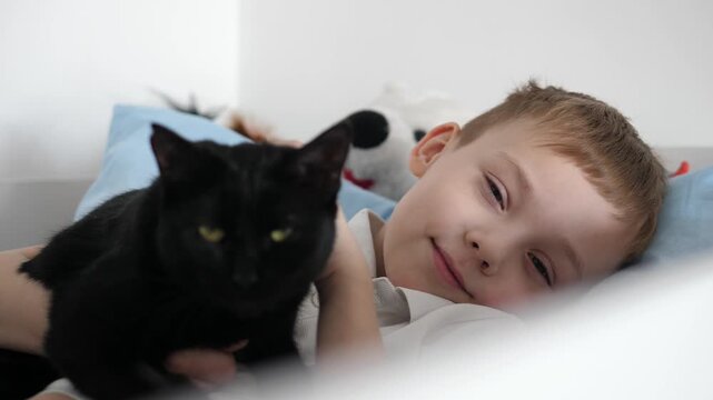 Happy little boy relaxing at home while cuddling his black cat. Warm, cozy family moment showing love, friendship and trust between child and pet.
