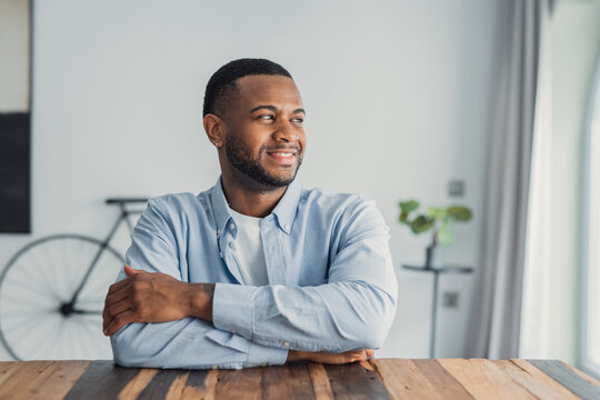 A stylish young Black man smiles while looking out the window, enjoying a quiet moment of reflection and visualizing personal success, confidence, and future opportunities in a modern headshot
