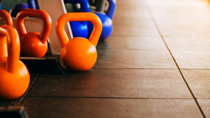 Orange kettlebell, black dumbbell, and ankle strap placed on gym floor, emphasizing strength training and fitness preparation.
