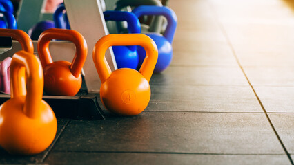 Orange kettlebell, black dumbbell, and ankle strap placed on gym floor, emphasizing strength training and fitness preparation.
