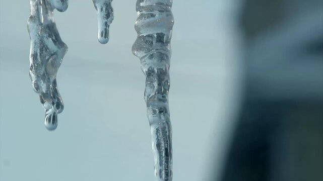 Closeup of melting icicles dripping from house gutters, forming an ice dam after a winter freeze, highlighting cold weather damage and home maintenance risks.