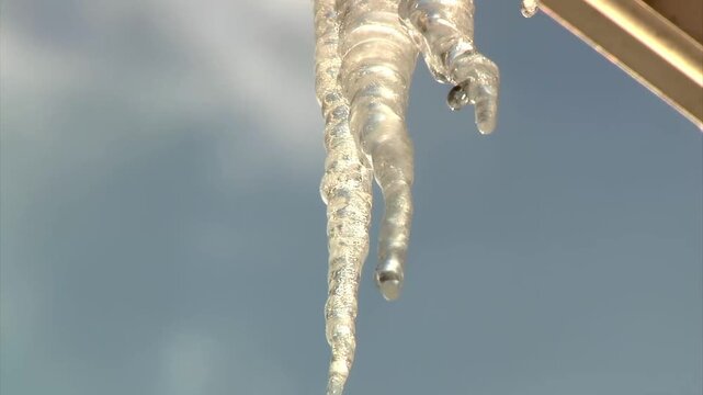 Closeup of melting icicles dripping from house gutters, forming an ice dam after a winter freeze, highlighting cold weather damage and home maintenance risks.