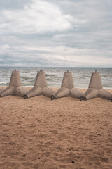 Fototapeta premium Tetrapods on the beach, Ukraine. Winter seascape with barrier blocks against russian invasion.Ukrainian coastal defense. Tetrapod in a row on sand. Seaside during war. Black Sea landscape 