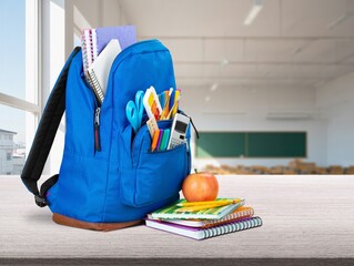 School backpack full of stuff  in classroom interior.