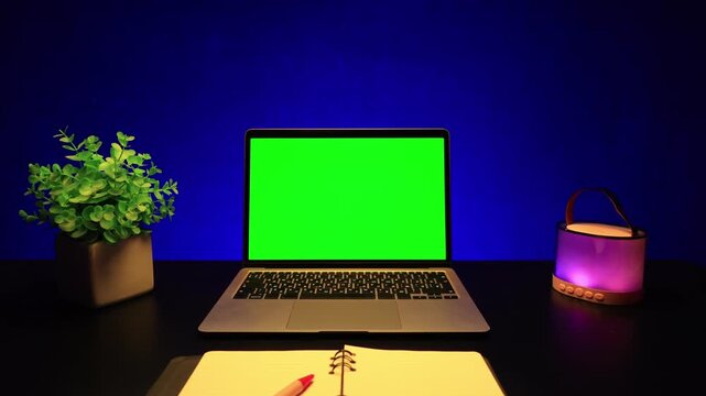 Modern desk setup with a laptop, notebook, and decorative lamp against a vibrant blue background