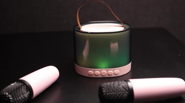 Portable Bluetooth speaker with colorful LED lights and two pink microphones on a dark background