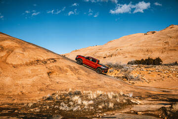 Off road pickup truck climbing steep sandstone slope in desert landscape at Sand Flats Recreation...