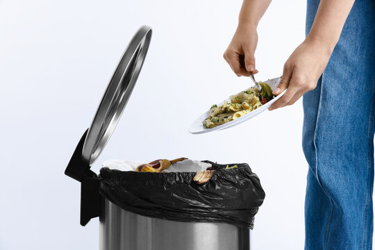 Woman throwing food waste into garbage can on white background, closeup