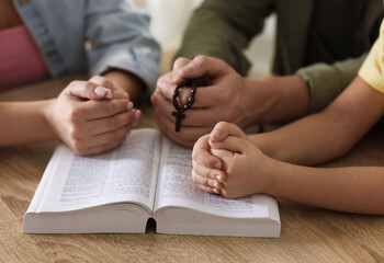 Obraz premium Family with Bible praying together at wooden table indoors, closeup