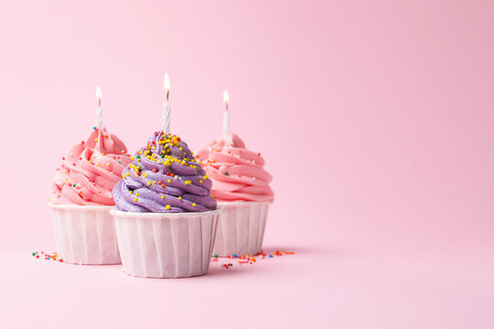 Yummy cupcakes with sprinkles and burning candles on pink background. Space for text