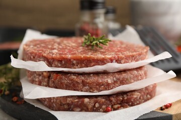Uncooked meat patties with rosemary and other products on table, closeup