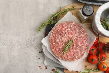 Uncooked meat patties with rosemary, tomatoes and other products on light grey table, flat lay....