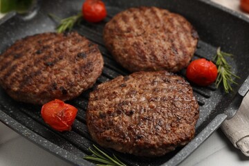 Delicious grilled meat patties, tomatoes and rosemary in grill pan on white tiled table, closeup
