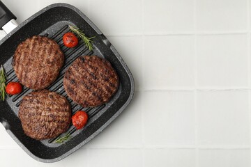 Naklejka premium Delicious grilled meat patties, tomatoes and rosemary in grill pan on white tiled table, top view. Space for text