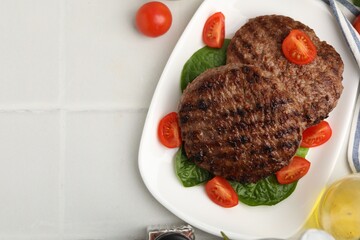 Naklejka premium Delicious grilled meat patties, tomatoes and spinach on white tiled table, flat lay. Space for text