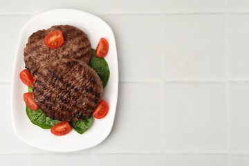 Naklejka premium Delicious grilled meat patties, tomatoes and spinach on white tiled table, top view. Space for text