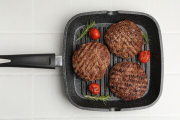 Naklejka premium Delicious grilled meat patties, tomatoes and rosemary in grill pan on white tiled table, top view