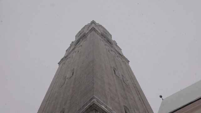 majestic "el Cianpan n" bell tower of the Basilica dei Santi Filippo e Giacomo rises above snow-covered rooftops in Cortina. Its stone facade and green clock glow against the winter sky.