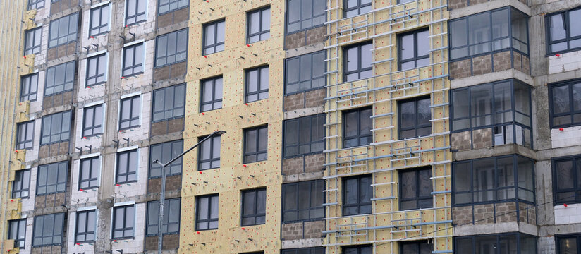 Urban construction site building facade with insulation material and metal framework for cladding, showing ongoing development and modern architecture progress in the city
