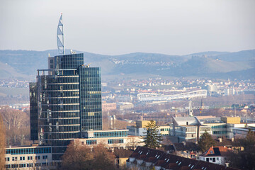 Modern glass skyscraper with distinctive triangular spire overlooking a cityscape, surrounded by hills and residential buildings in the background