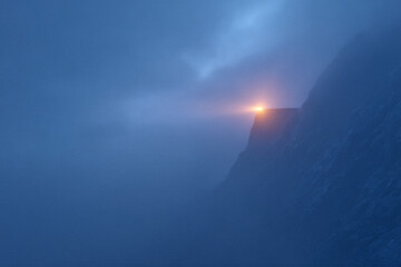 Obraz premium Mysterious mountain beacon illuminates foggy cliffside at night