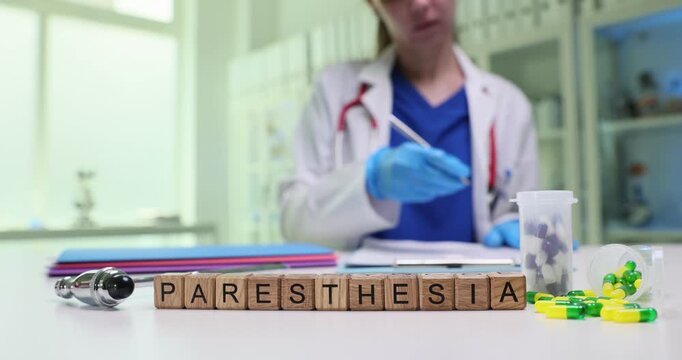 Wooden cubes spell word Paresthesia on bright medical desk. Female neurologist writes report while evaluating numbness symptom history in clinic