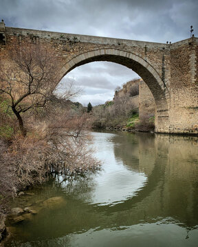 Ancient stone arch bridge over the River Tajo on a cloudy day, Toledo, Castile-La Mancha, Spain, January 2020