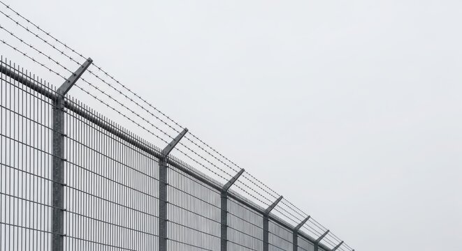 Barbed wire on top of a metal fence against a clear sky. Security and boundary concept for restricted areas.