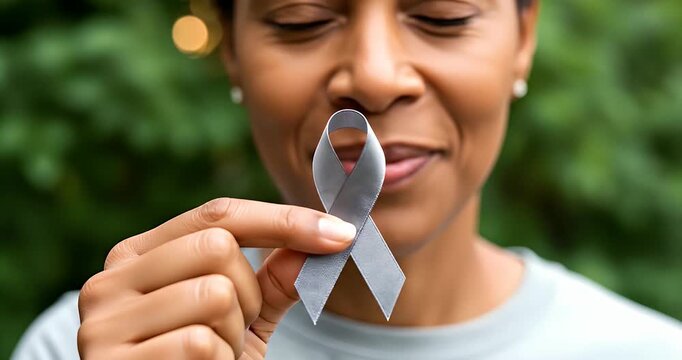 A woman gently holds a gray awareness ribbon near her mouth, symbolizing support for a cause.