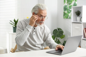 Unhappy senior man feeling fatigue at white table indoors