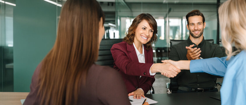 Group of corporate people happy with results of team work at meeting. Mature worker woman shaking hand with client, recruit employee or business partner after signing contract. Web banner, copy space