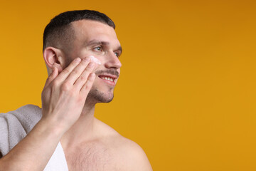 Fototapeta premium Handsome man applying cream onto his face against yellow background. Space for text