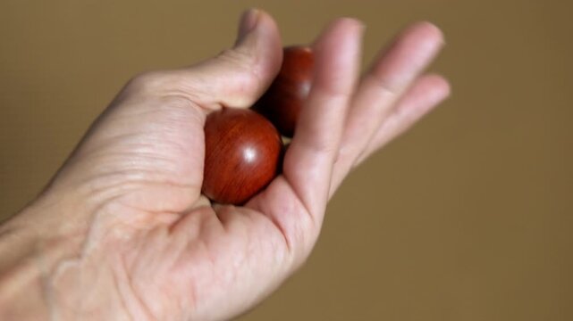 Hand exercising rotating two wooden baoding balls. Man's hand rotating two wooden chinese meditation balls for stress relief, physical therapy, and improving dexterity, promoting relaxation