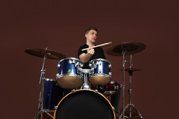 Man playing drums with drumsticks on brown background, low angle view