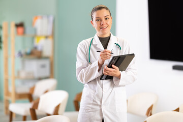 Girl medical receptionist with tablet greets guests, invites them to pass, indicates direction of...