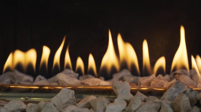 Detailed close-up of a row of vibrant yellow flames emerging from a gas burner tube, surrounded by white decorative pebbles in a modern
