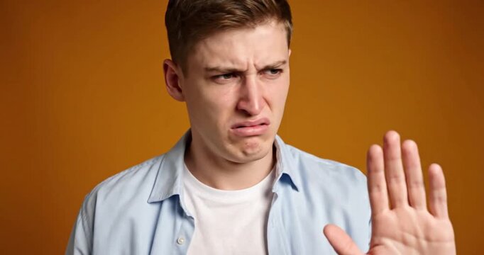 Young Man Expressing Disgust and Aversion on Warm Studio Background
