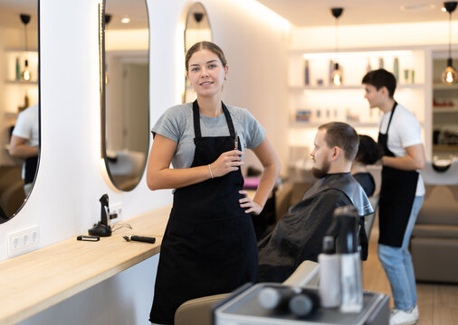 Young female hairdresser stylist posing with scissors in beauty salon