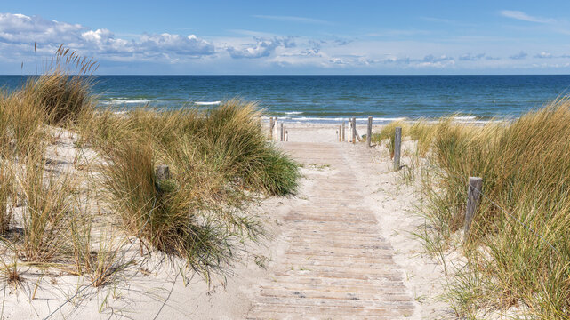 Holzweg durch D&uuml;nen mit Strandhafer zum Strand der Ostsee mit blauem Himmel mit Wolken. Ostseebad Rerik in Mecklenburg-Vopmmern, Deutschland