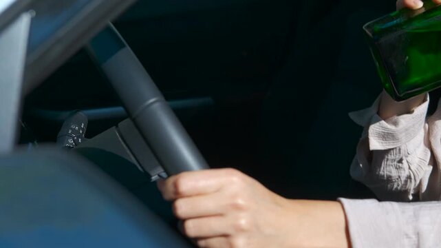 Woman drinking alcohol while driving a car. Female driver gripping steering wheel while holding green alcohol bottle, symbolizing reckless driving and serious road safety violation