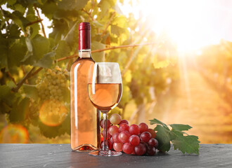 Naklejka premium Wine and fresh grapes on table. Glass and bottle in sunny vineyard