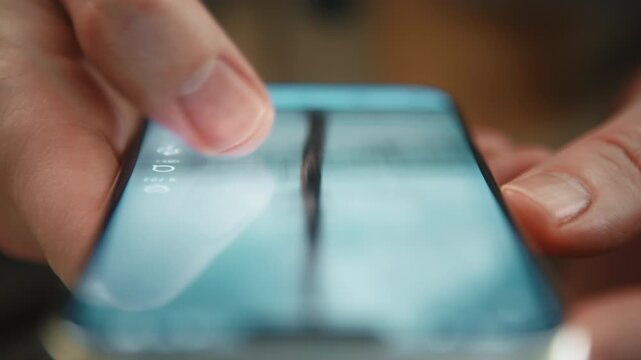 Extreme close-up male hand in warm colored shirt scrolling social media feed on smartphone indoors. Swiping finger, motion blur on phone screen. Online browsing, digital content consumption, daylight