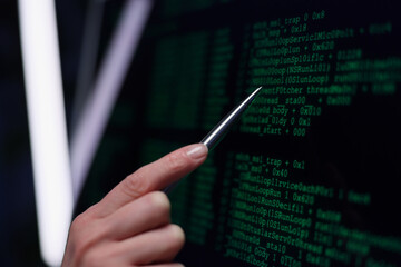 A skilled individual points intently at vibrant green code displayed on a dark screen, surrounded by modern technology. The scene highlights focus on coding intricacies during nighttime. © H_Ko