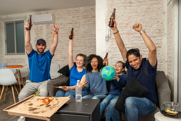 Fototapeta premium Family and friends celebrating a football soccer moment at home while eating pizza and drinking beverages together, smiling and cheering in front of the TV. Sports joy, friendship, home gathering